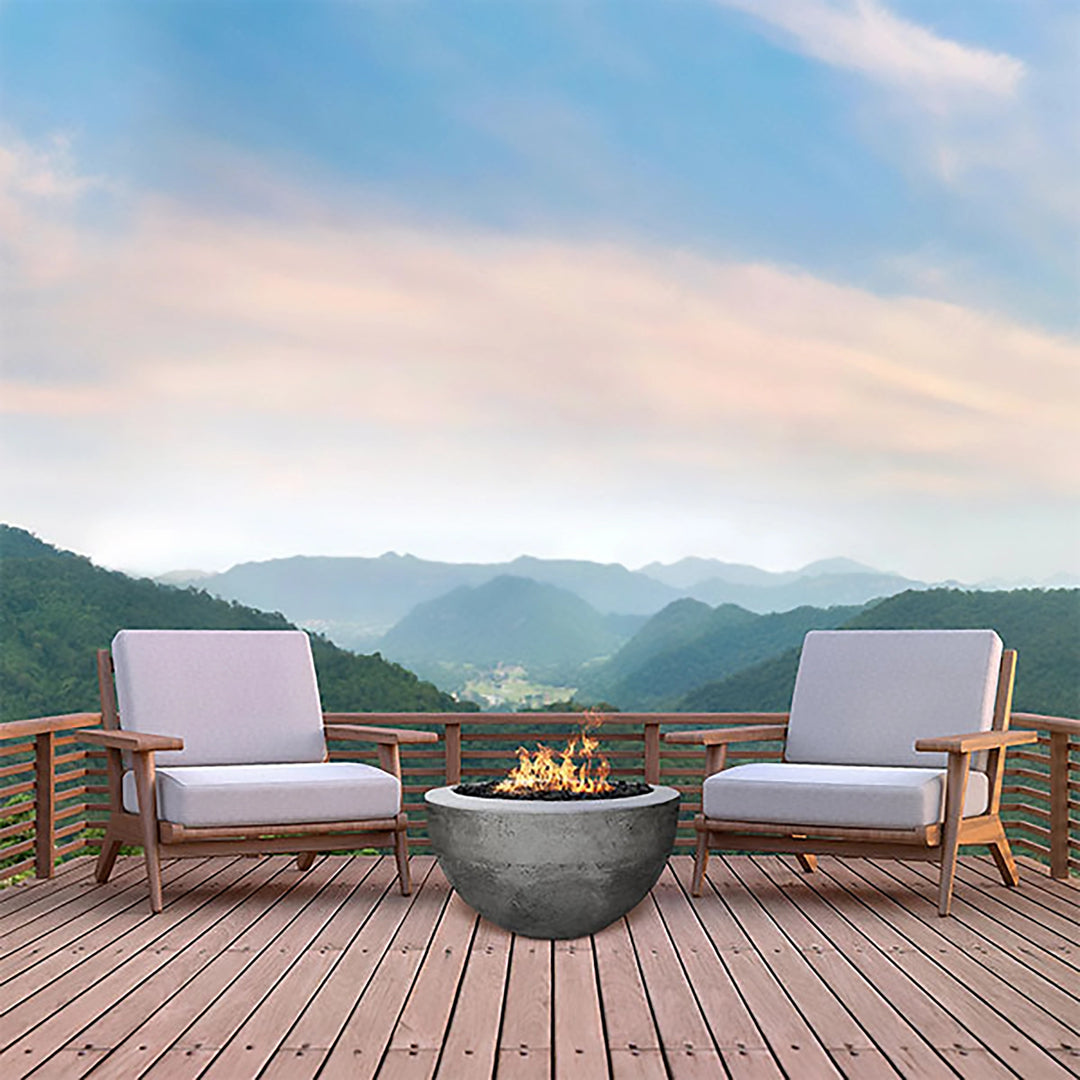 Prism Hardscapes Moderno 3 Gas Fire Bowl in a serene mountaintop setting, surrounded by sleek wooden deck furniture. The natural gray concrete fire bowl offers a beautiful contrast against the backdrop of rolling hills and a pastel sky, creating a peaceful and inviting outdoor space. Perfect for luxury outdoor fire pits on decks, patios, or large backyard settings. 