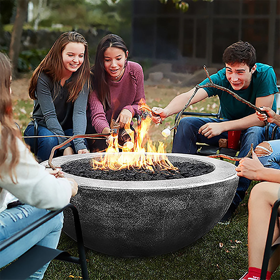 A group of friends enjoying a cozy evening around the Prism Hardscapes Moderno 4 Gas Fire Pit. The concrete fire bowl, finished in a natural texture, provides the perfect ambiance for roasting marshmallows and gathering outdoors. Suitable for propane or natural gas setups.