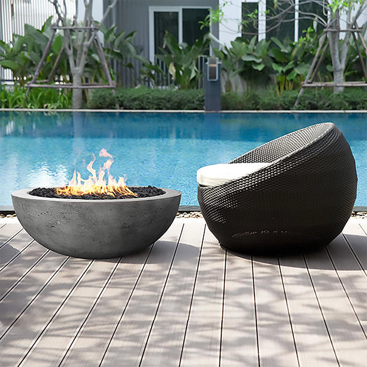 A modern outdoor setting featuring the Prism Hardscapes Moderno 4 Gas Fire Pit next to a luxurious pool. The sleek, contemporary design of the concrete fire bowl in pewter finish complements the relaxing poolside seating area. Perfect for propane or natural gas outdoor fire pits.