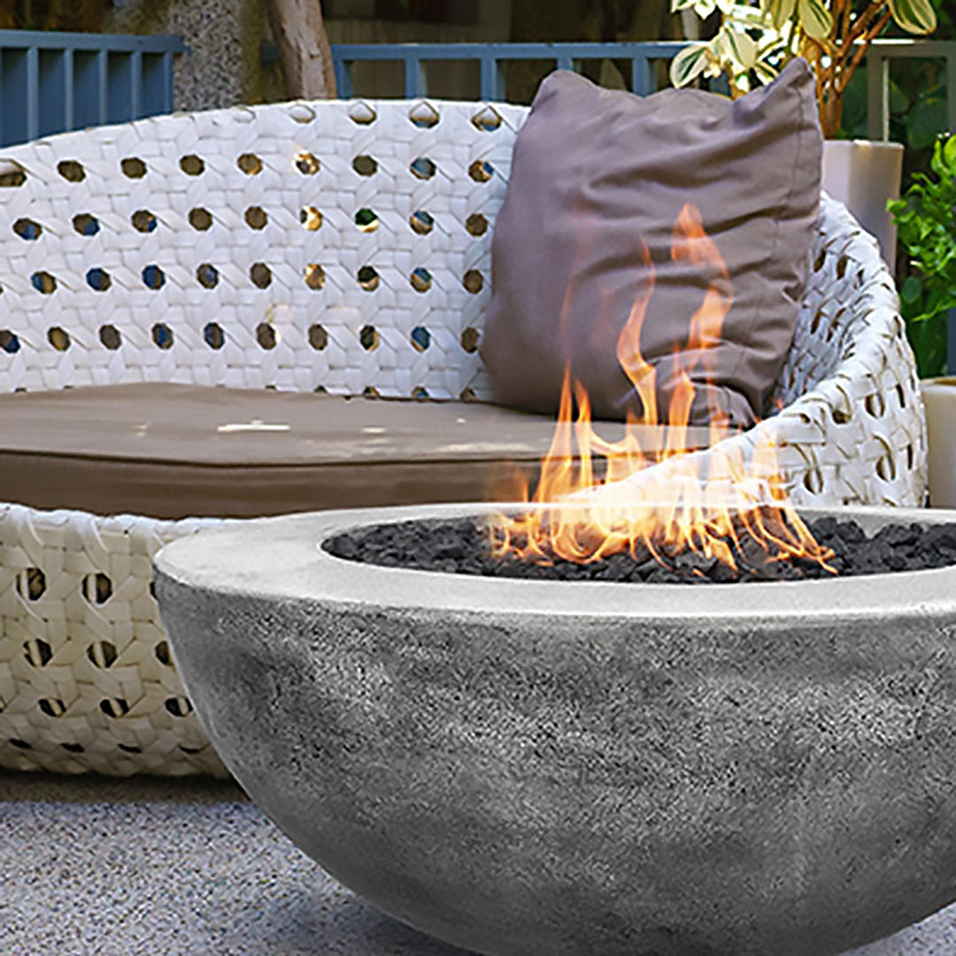 This image showcases the Prism Hardscapes Moderno 5 Gas Fire Bowl in a stunning pewter finish, enhancing the ambiance of a stylish outdoor seating area. The fire pit, surrounded by cozy wicker lounge furniture, emits soft flames over black lava rocks, making it an ideal modern fire pit for outdoor spaces. Perfect for contemporary patios or backyards, this fire pit brings warmth and style.