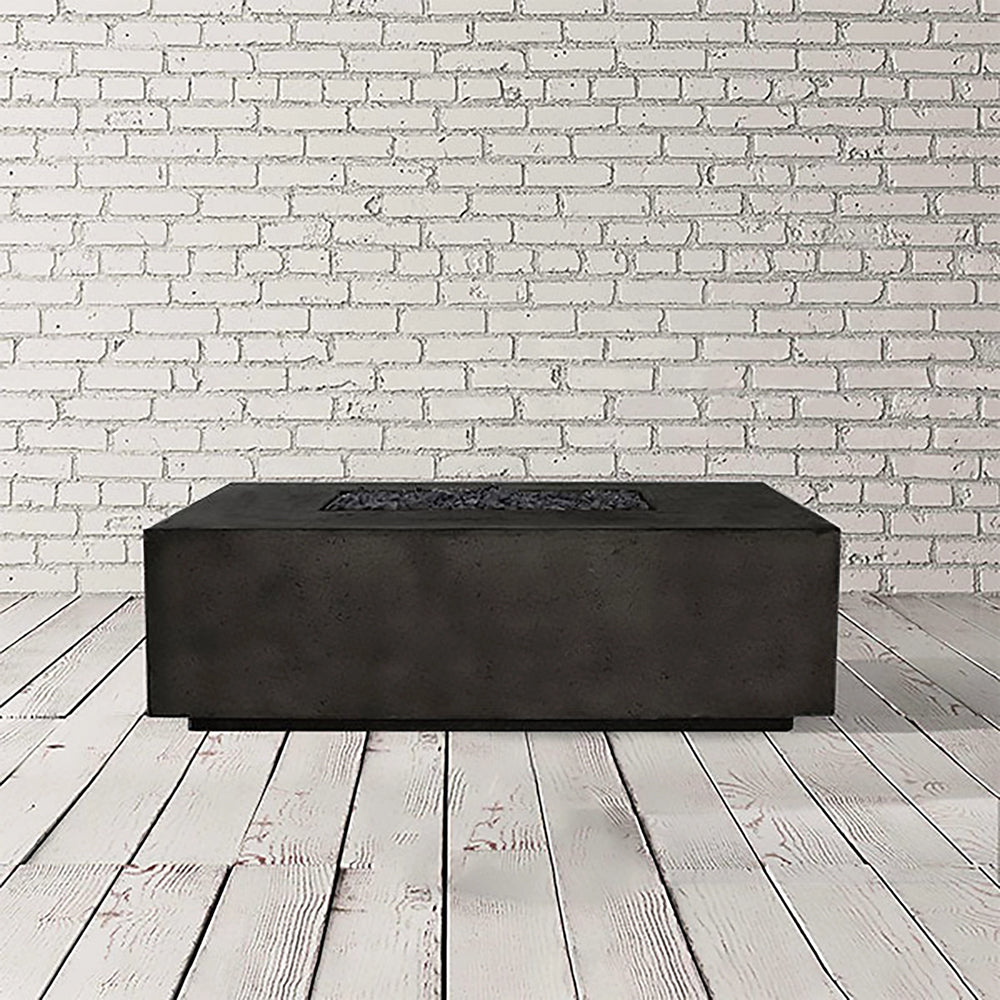 The Prism Hardscapes Portos 68 Propane Fire Table in an ebony finish, shown in a studio setting with a white brick background. The fire table features a modern rectangular design and a smooth, flat surface, perfect for a contemporary outdoor space. The dark ebony color adds an element of sophistication, making this fire table an ideal centerpiece for luxury patio settings. A great addition for creating a warm and inviting outdoor atmosphere. 