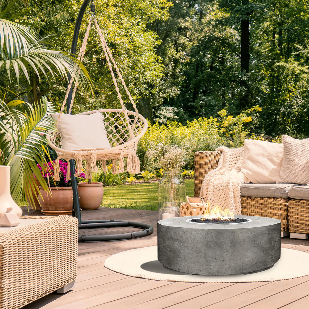 The Prism Hardscapes Rotondo Gas Fire Pit in Natural provides a sleek, round centerpiece to this cozy patio setup. Paired with a natural chair and modern furniture, it complements the outdoor living space beautifully. This concrete fire pit is ideal for creating warmth in outdoor spaces, backyard designs, and modern patios. It operates on natural gas and includes lava rocks for a balanced mix of style and function, perfect for outdoor fire pit settings, modern fire pits, and outdoor gatherings.