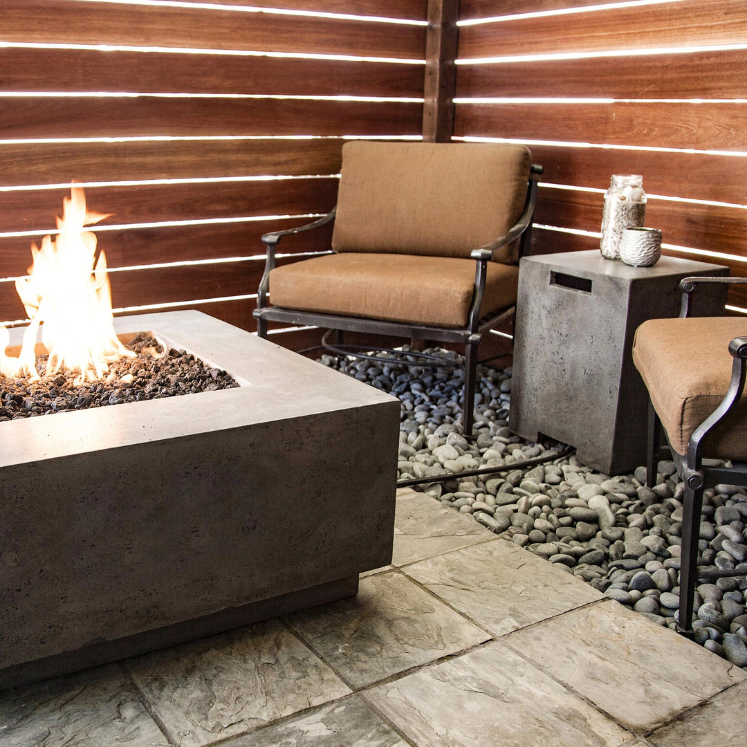 Prism Hardscapes Sausalito Propane Tank Enclosure shown in a cozy patio setting next to a modern fire pit, blending natural stone and concrete textures. The durable propane tank cover adds a sleek and functional element to the outdoor space. Ideal for backyard fire pit setups, outdoor fire table settings, or patio gatherings. The enclosure complements the natural surroundings, creating an inviting atmosphere for relaxation.