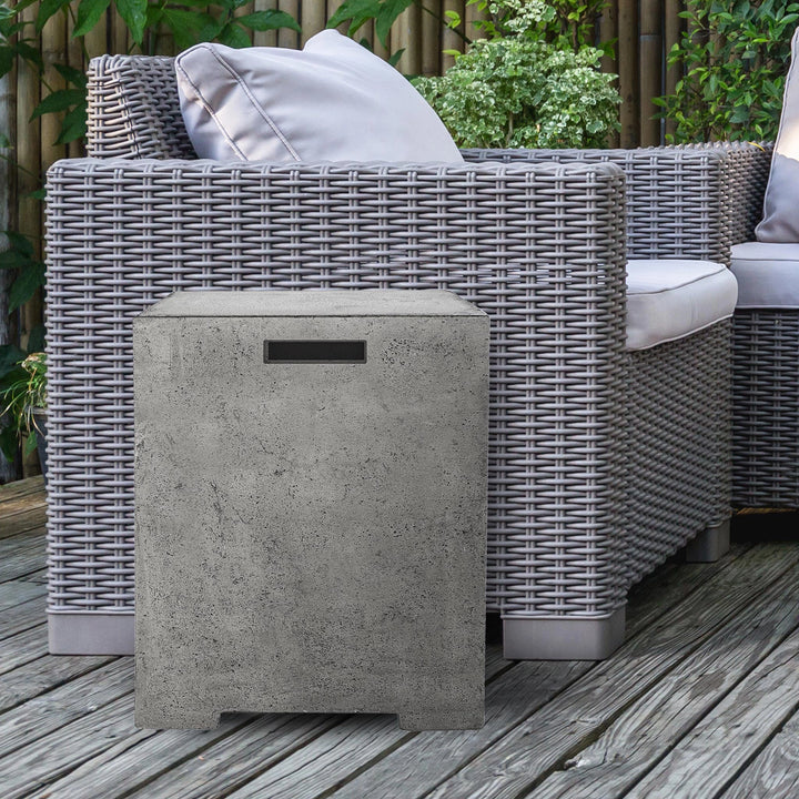 Prism Hardscapes Sausalito Propane Tank Enclosure displayed next to a modern wicker patio chair, showcasing its neutral concrete texture and compact design. The enclosure seamlessly fits into outdoor patio furniture arrangements, providing a discreet and durable housing for the propane tank. Perfect for outdoor fire pit areas or backyards with stylish seating arrangements, adding both function and form to the space