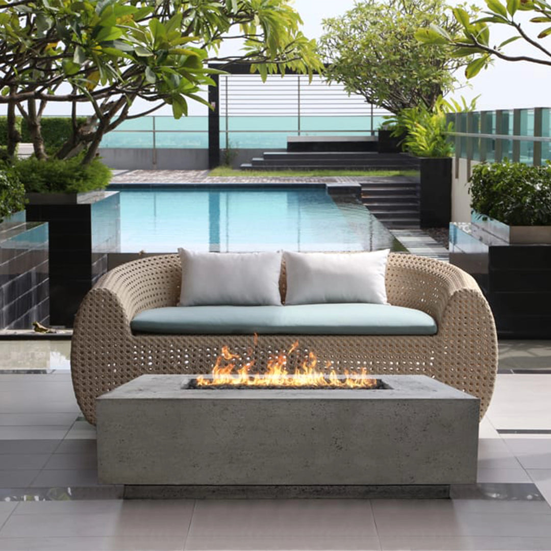 Prism Hardscapes Tavola 1 Gas Fire Pit in natural gray, set against a modern lounge area by the pool. The contemporary design of the fire pit complements the cozy seating arrangement, making it an inviting focal point for outdoor living spaces. This rectangular natural gas fire pit offers a sophisticated way to enjoy warmth and relaxation outdoors.