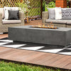 The Prism Hardscapes Tavola 4 Gas Fire Pit is featured in a cozy garden lounge, surrounded by wicker chairs and colorful cushions. The rectangular fire pit, with its sturdy concrete design, complements the natural garden setting while providing a warm and inviting flame. This gas fire pit is ideal for backyard gatherings, creating a focal point for outdoor entertainment. 