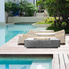 The Prism Hardscapes Tavola 4 Gas Fire Pit is elegantly positioned by a serene poolside, complementing the luxurious outdoor setting with its sleek, modern rectangular design. The fire pit features a natural concrete finish that seamlessly blends with the surrounding environment, offering a relaxing atmosphere for lounging. Perfect for outdoor spaces near water, this gas fire pit elevates poolside décor. 