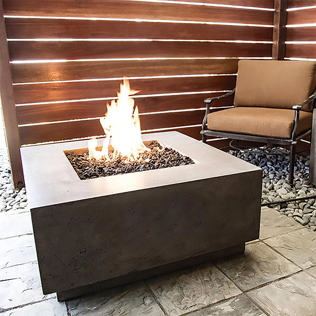 A cozy private patio with the Prism Hardscapes Tavola 42 Gas Fire Pit igniting a beautiful flame over dark lava rocks. The rich pewter finish of the fire pit complements the natural tones of the patio's wooden accents, creating a warm and intimate atmosphere. Perfect for small spaces, this gas fire pit adds both comfort and modern style, making it ideal for personal relaxation or social gatherings