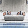 A contemporary poolside lounge setup featuring the Prism Hardscapes Tavola 5 Gas Fire Pit. The sleek fire pit is surrounded by modern seating, creating a luxurious ambiance for relaxation. Its rectangular design and smooth concrete surface blend effortlessly with the sophisticated décor of the lounge, making it a must-have for high-end outdoor living spaces. 