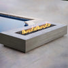 The Prism Hardscapes Tavola 6 Gas Fire Pit elegantly positioned beside a modern pool, flames adding a touch of luxury to the outdoor area. The concrete fire pit complements the minimalist poolside design, perfect for evening gatherings and relaxation. A sleek design ideal for enhancing backyard spaces with both style and function. 