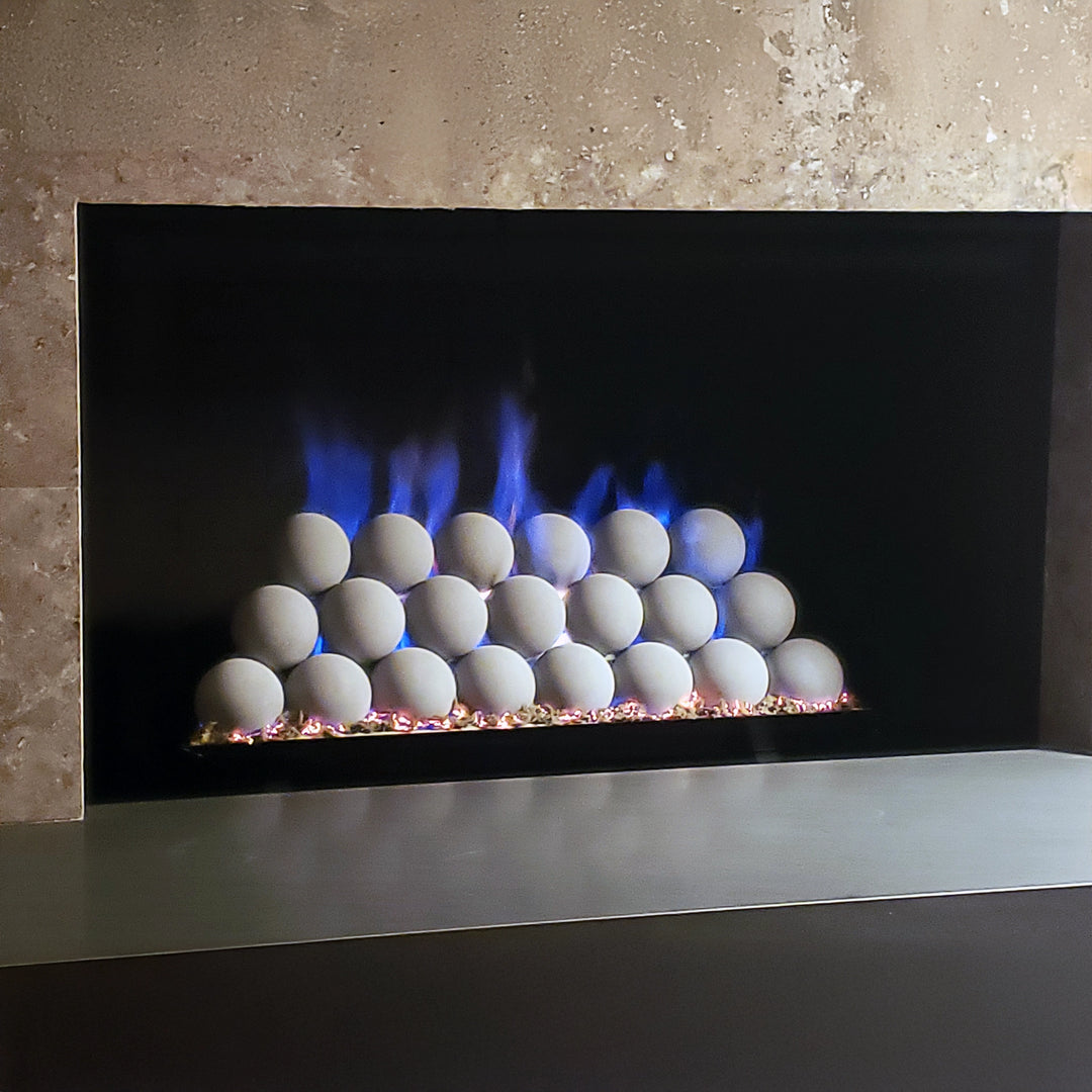 Rasmussen vented uniform fireballs set arranged neatly in a modern fireplace with a sleek, minimalist design. Blue flames accentuate the evenly stacked white fireballs, creating a stunning centerpiece. This vented fireball set is perfect for contemporary indoor fireplaces and enhances any modern living space with a unique fire feature. Ideal for large fire pits, luxury fire pits, and modern gas fireplaces, this setup highlights the beauty of clean, symmetrical lines and fire elegance.