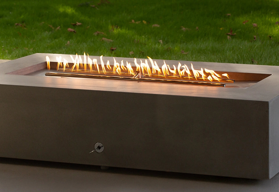 Modern rectangular concrete gas fire pit with a stainless steel linear burner, producing bright flames for an elegant outdoor heating solution.