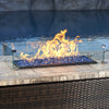 The American Fireglass Rectangular Glass Flame Guard is elegantly displayed on a wicker-style outdoor table, positioned by the poolside. The clear glass guard enhances flame stability while protecting the fire from wind, ensuring a vibrant and consistent flame over beautiful blue fire glass. This flame guard is a perfect accessory for outdoor fire pits, adding both safety and modern style to any poolside or patio fire table setup.