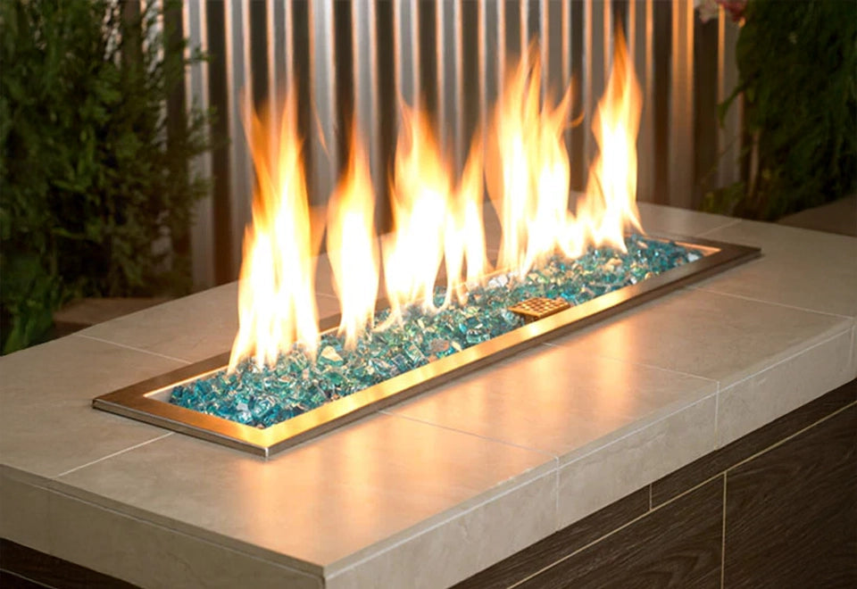 Sleek rectangular stainless steel drop-in fire pit burner showcasing vibrant flames over shimmering blue fire glass media. Ideal for custom gas fire pit installations, offering a modern and stylish addition to outdoor patio spaces and built-in fire features.