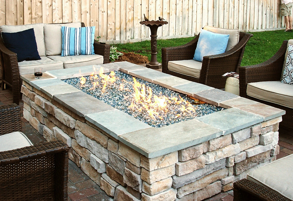 Rectangular stone fire pit with a fire glass burner, creating a warm ambiance for an outdoor patio with wicker seating.