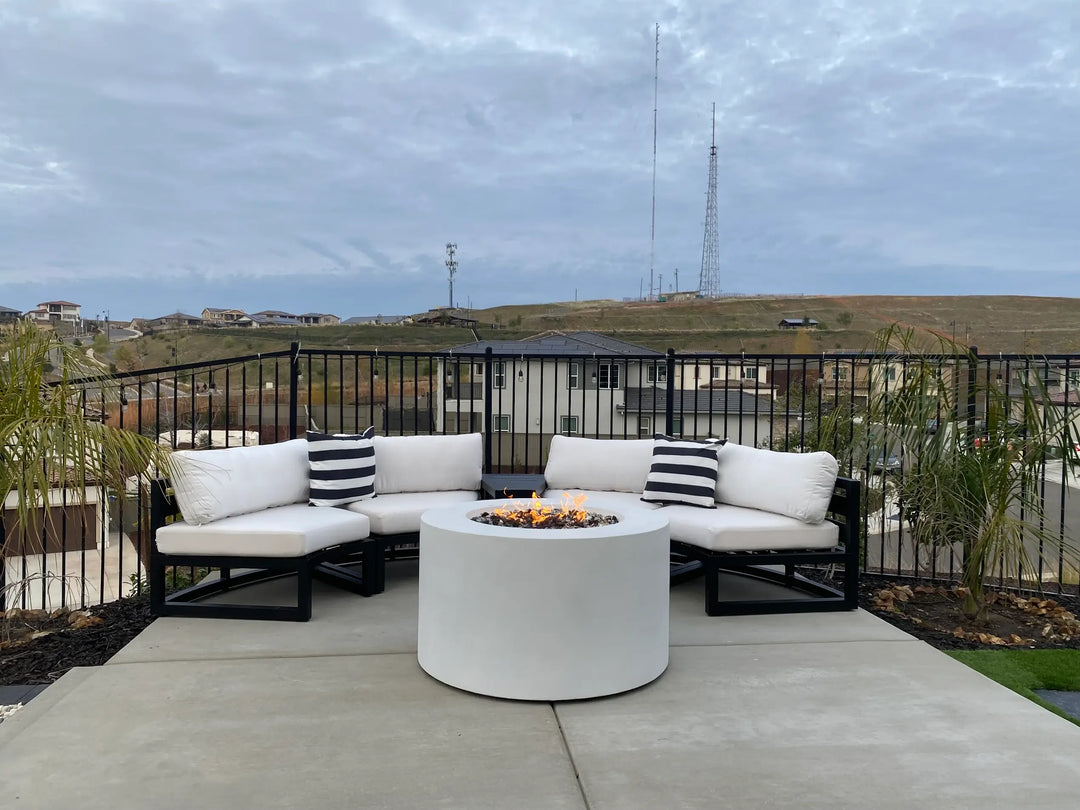 A steel fire pit with a white powder coat finish is showcased on a backyard patio overlooking the neighborhood, surrounded by a round patio furniture sectional.
