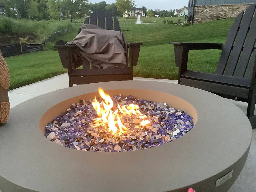 Premixed ocean fire glass is on display in a round concrete fire pit bowl overlooking a large grass backyard.