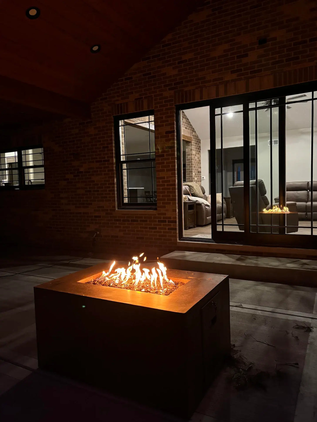 A steel fire pit is lit at night in a backyard on a customer's patio