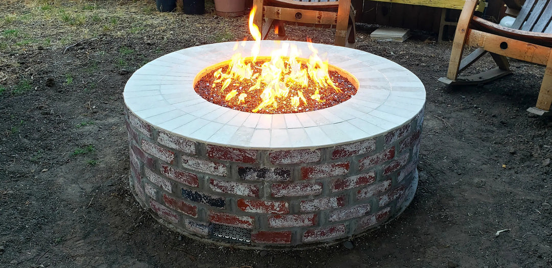 A custom brick inlay fre pit showcasees red broken fire glass ignited in the backyard.