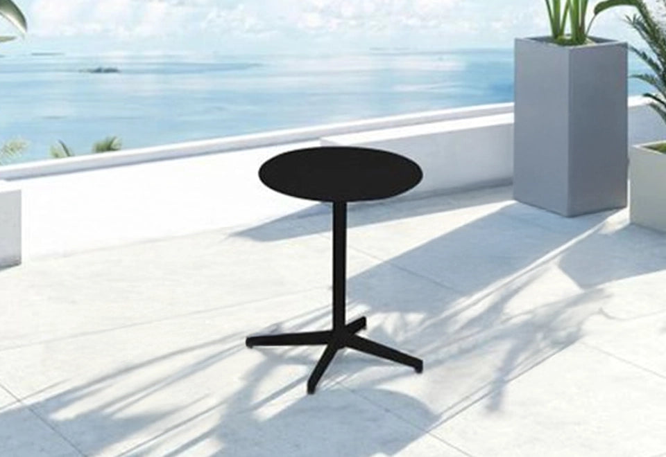 Minimalist black round bistro table with a sturdy base on a modern balcony, offering a serene ocean view with contemporary gray planters and tropical greenery.