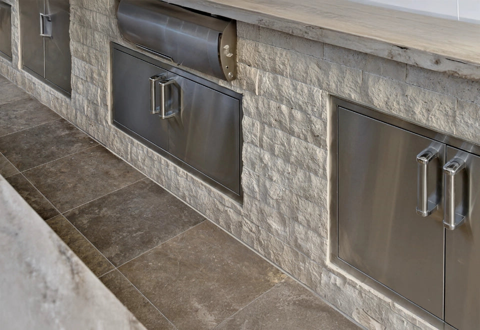 Outdoor kitchen with stainless steel BBQ island doors and drawers set against a textured stone facade, offering durable storage and access for grilling essentials.