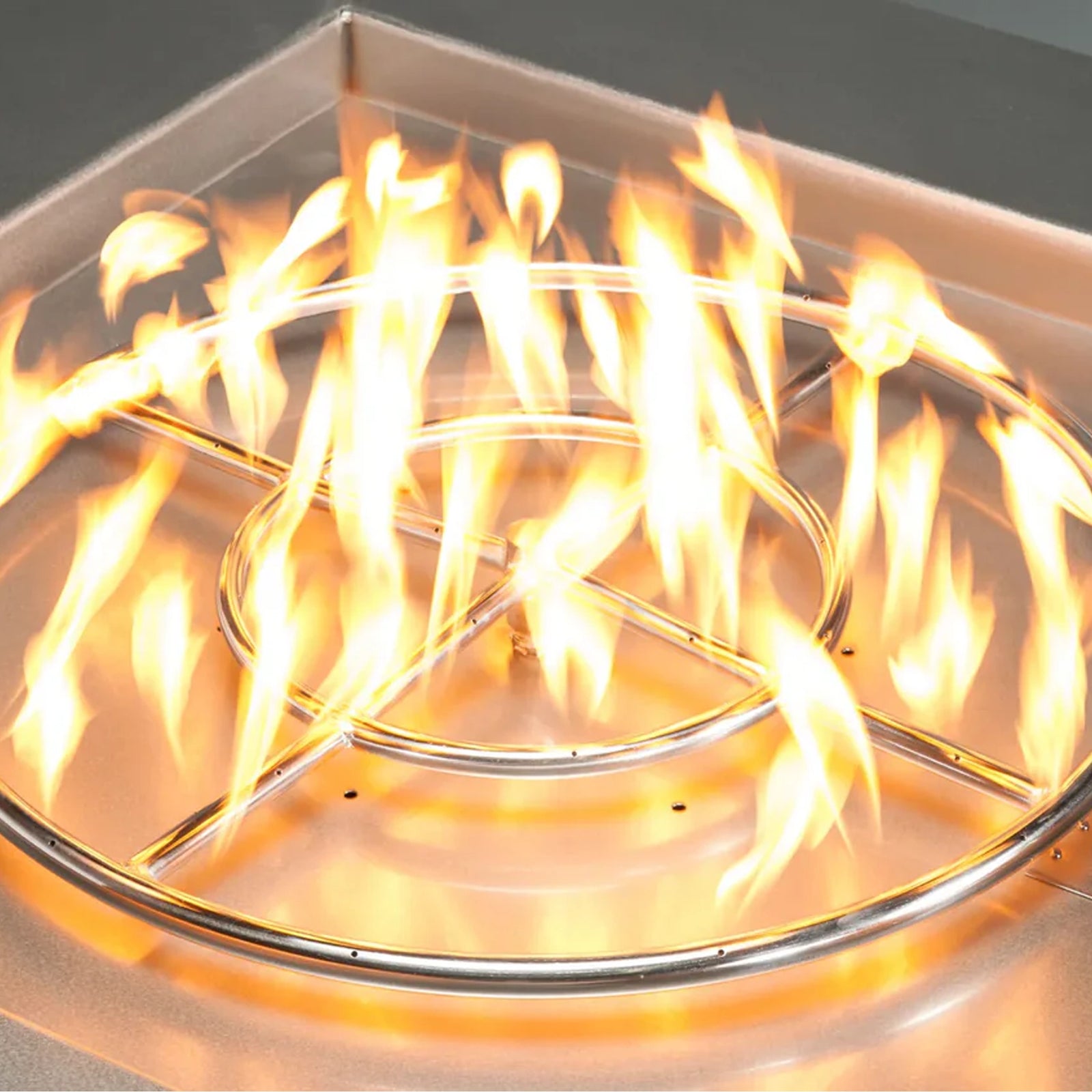 Close-up of a stainless steel circular fire pit burner with evenly distributed flames, providing an intense and warm ambiance for outdoor gatherings