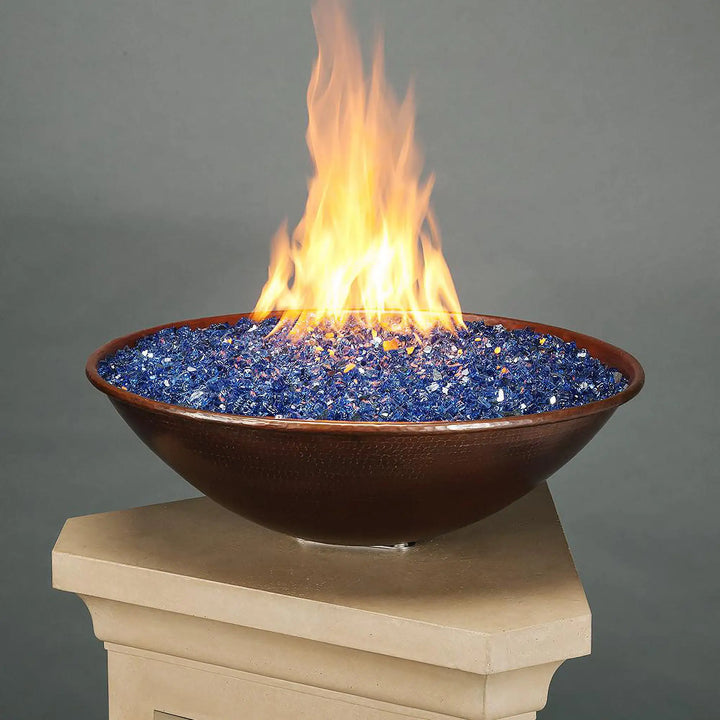 Taza Moreno 30-inch round copper fire and water bowl with blue fire glass and bright flames, elegantly displayed on a stone pedestal, ideal for modern outdoor spaces by Starfire Designs