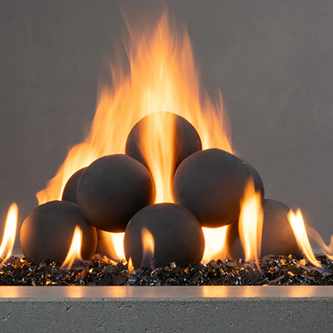 Close-up of Starfire Designs 4-inch ceramic fire balls set of 12 in dark gray, surrounded by intense flames from a fire pit. The smooth, spherical surfaces of the fire balls offer a bold and refined look for any gas fire feature.