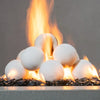 Close-up view of 12 white ceramic fire balls from Starfire Designs, each 4 inches in diameter, arranged in a pyramid and surrounded by flickering flames. The fireballs are displayed on a bed of black fire glass, creating a striking contrast that enhances the elegance of the fire feature. Perfect for modern gas fire pits, these ceramic fireballs are heat-resistant and designed for outdoor use. Ceramic fireballs, fire glass, modern fire pit design, white fire pit feature