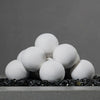 Close-up of 12 white 4-inch ceramic fire balls by Starfire Designs arranged on top of black fire glass in an unlit fire pit. The ceramic fireballs create a clean and modern aesthetic, ideal for enhancing the look of gas fire pits in outdoor spaces. These heat-resistant fireballs are durable and suitable for both residential and commercial fire features. White ceramic fireballs, modern fire pit décor, gas fire pit accessory, outdoor fire feature.