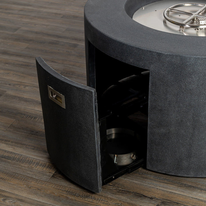 Close-up of the Starfire Designs Beton 42-inch Graphite Round Concrete Gas Fire Pit with the access door open, revealing the hidden compartment for the propane tank. This fire pit offers an elegant yet functional design with a smooth concrete finish and stainless steel internal components.