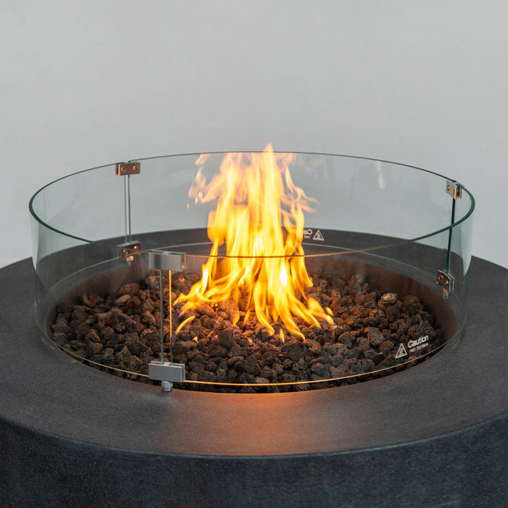 Close-up view of the flickering flame within the Starfire Designs Beton 42-inch Graphite Round Concrete Gas Fire Pit, featuring the protective glass wind guard and lava rocks for added visual appeal. Ideal for creating a cozy outdoor setting.