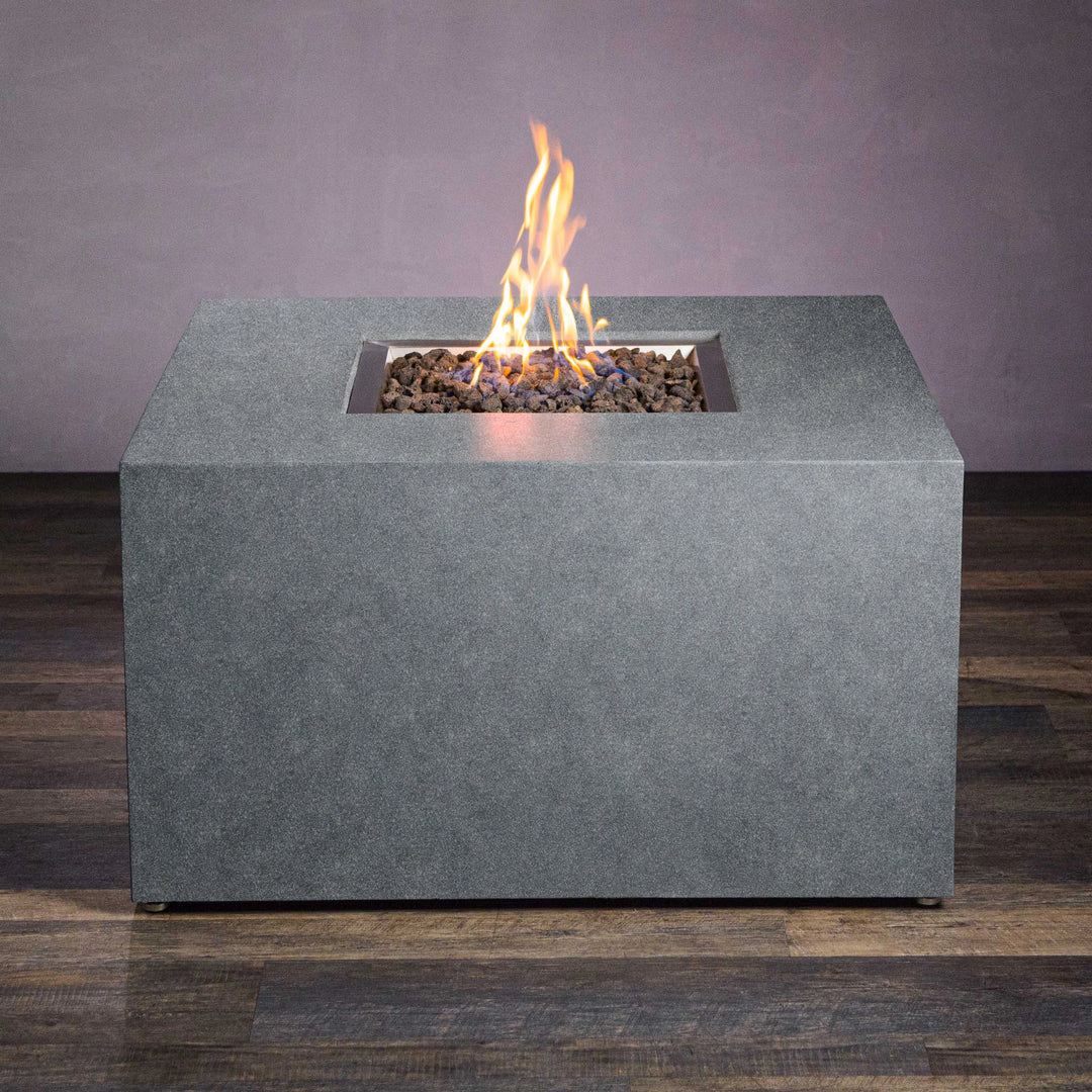 A detailed view of the Starfire Designs Beton 42" Graphite Square Hidden Propane Tank Gas Fire Pit without flames. The sleek and minimalist design in graphite gray enhances its modern appeal, with a flat top surface surrounding a central fire bowl filled with lava rocks. This weather-resistant fire pit features durable concrete construction, suitable for all-season outdoor use.