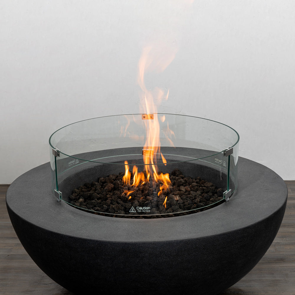 The Starfire Designs Beton 42 Inch Graphite Round Concrete Natural Gas Fire Pit with a glowing flame surrounded by a tempered glass wind guard, combining safety, modern aesthetics, and optimal heat output for outdoor gatherings.