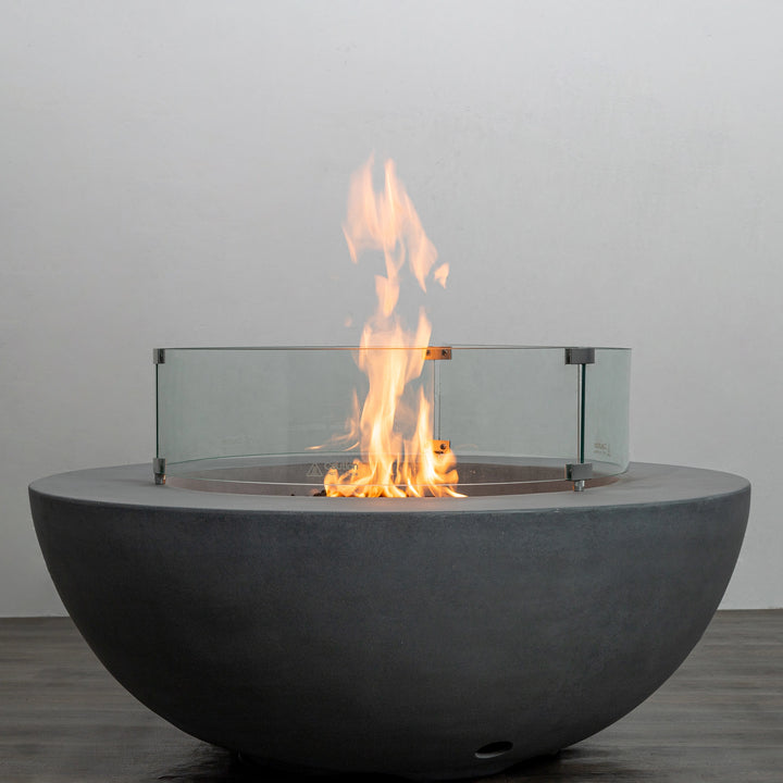 The Starfire Designs Beton 42 Inch Natural Gray Round Concrete Natural Gas Fire Pit with Push Button Ignition, equipped with a tempered glass wind guard for enhanced flame stability. A sophisticated addition to outdoor fire tables and backyard setups