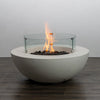 Starfire Designs Beton 42 Inch White Round Concrete Gas Fire Pit lit with flames inside a glass wind guard, creating an elegant and modern ambiance for outdoor gatherings.