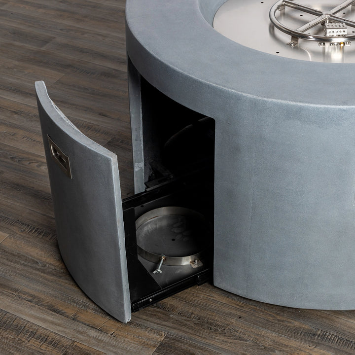 A close-up shot of the Starfire Designs Beton 42" Natural Gray Round Concrete Gas Fire Pit showing the open access door and the internal burner structure. The premium stainless steel burner adds to the durability, while the natural gray finish complements any outdoor aesthetic.