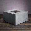 Starfire Designs Beton 42" Natural Gray Square Gas Fire Pit, unlit, displaying its clean and smooth concrete body. The minimalist square design makes this fire pit an ideal choice for modern outdoor settings. Lava rocks surround the burner, enhancing the aesthetic appeal even when not in use. This fire pit features hidden propane tank storage for a seamless look.