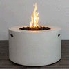 A bright, steady flame rises from a bed of dark lava rocks in a white round fire pit, the smooth cylindrical body of this concrete fire pit standing on a dark wood-look floor against a simple backdrop; the clean lines and integrated side handles highlight a sleek modern fire pit design, while the recessed burner of this gas fire pit delivers consistent, adjustable warmth for contemporary outdoor or semi-enclosed living spaces.