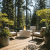 On a sunlit cedar deck surrounded by tall evergreens, a white round fire pit glows at the center of four cushioned lounge chairs, its concrete fire pit bowl filled with lava rocks as flames flicker gently; the setup suggests a fire pit safe for wood deck use, creating a tranquil, cozy backyard fire pit retreat where guests can unwind, sip drinks, and enjoy forest views without leaving the comfort of their elevated outdoor room.