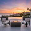 At dusk on a pale stone patio beside an infinity pool, four dark wooden Adirondack chairs are spaced around a low charcoal rectangular fire pit, the long outdoor fire pit containing a channel of dark stones and continuous yellow flames, with steps, small lights, and distant hills framing the view, so the symmetrical seating and central glow make the setup resemble a backyard fire pit designed as a simple family gathering fire pit overlooking the valley.