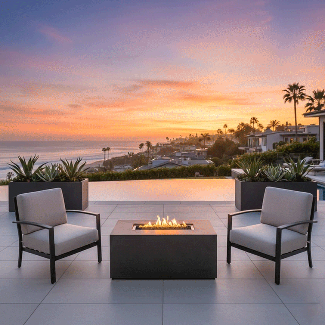 At dusk on a pale stone patio beside an infinity pool, four dark wooden Adirondack chairs are spaced around a low charcoal rectangular fire pit, the long outdoor fire pit containing a channel of dark stones and continuous yellow flames, with steps, small lights, and distant hills framing the view, so the symmetrical seating and central glow make the setup resemble a backyard fire pit designed as a simple family gathering fire pit overlooking the valley.