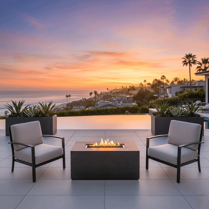 At dusk on a pale stone patio beside an infinity pool, four dark wooden Adirondack chairs are spaced around a low charcoal rectangular fire pit, the long outdoor fire pit containing a channel of dark stones and continuous yellow flames, with steps, small lights, and distant hills framing the view, so the symmetrical seating and central glow make the setup resemble a backyard fire pit designed as a simple family gathering fire pit overlooking the valley.