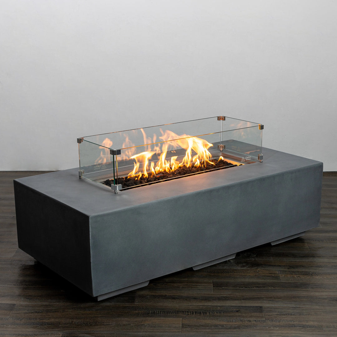 Flames roaring within the Starfire Designs Beton 55-inch natural gray rectangle gas fire pit, with the glass wind guard securely framing the fire, creating a stunning and modern outdoor focal point. This setup adds both functionality and safety for outdoor gatherings