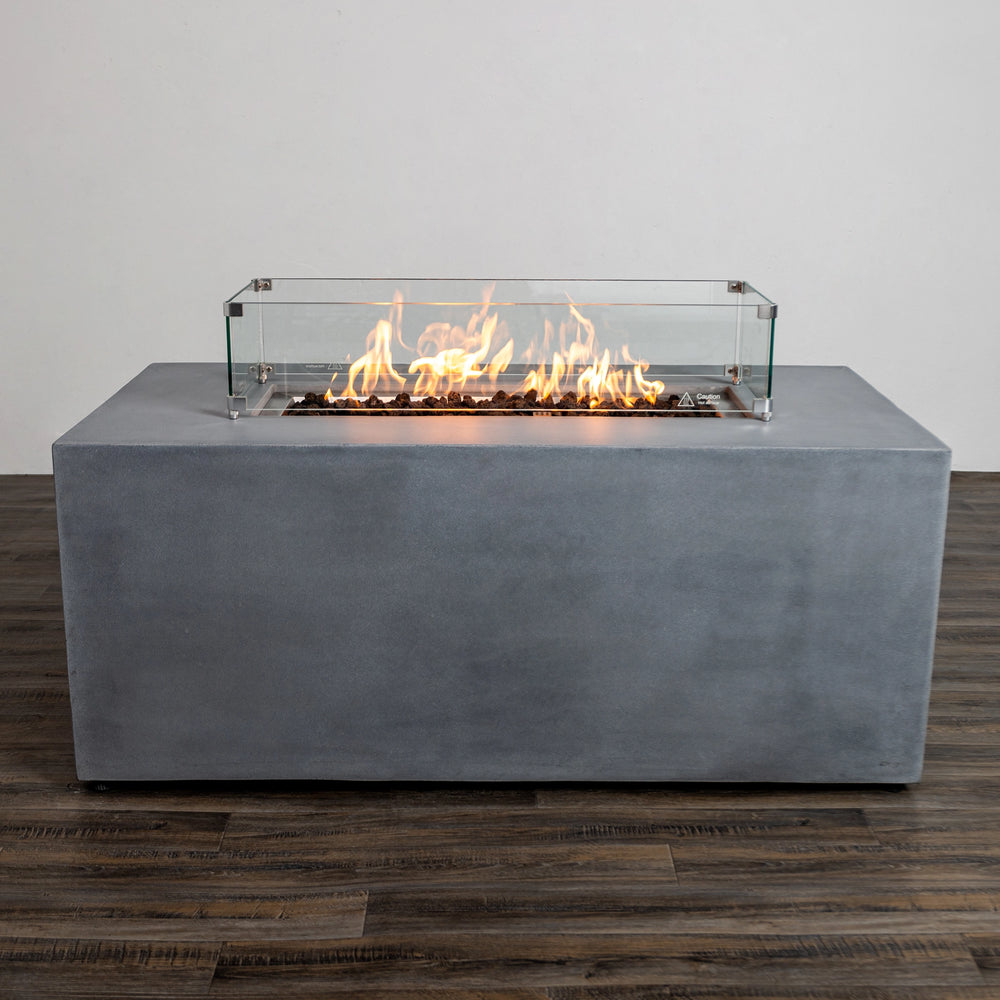 Full front view of the Starfire Designs Beton 55" Natural Gray Rectangle Hidden Propane Tank Gas Fire Pit with flames glowing inside the tempered glass wind guard. The glass enclosure enhances safety and adds elegance to the modern fire pit design, perfect for outdoor entertaining.