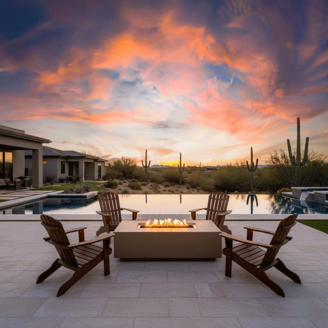 On a pale stone patio beside an infinity pool that blends into a desert horizon, four wooden Adirondack chairs form a circle around a low sand-colored concrete fire pit, its long rectangular burner sending steady flames above dark lava rocks as tall saguaro cacti and a vivid pink-and-orange sunset sky frame the scene, turning the space into a relaxed backyard fire pit setting that feels like a private backyard oasis in the desert.