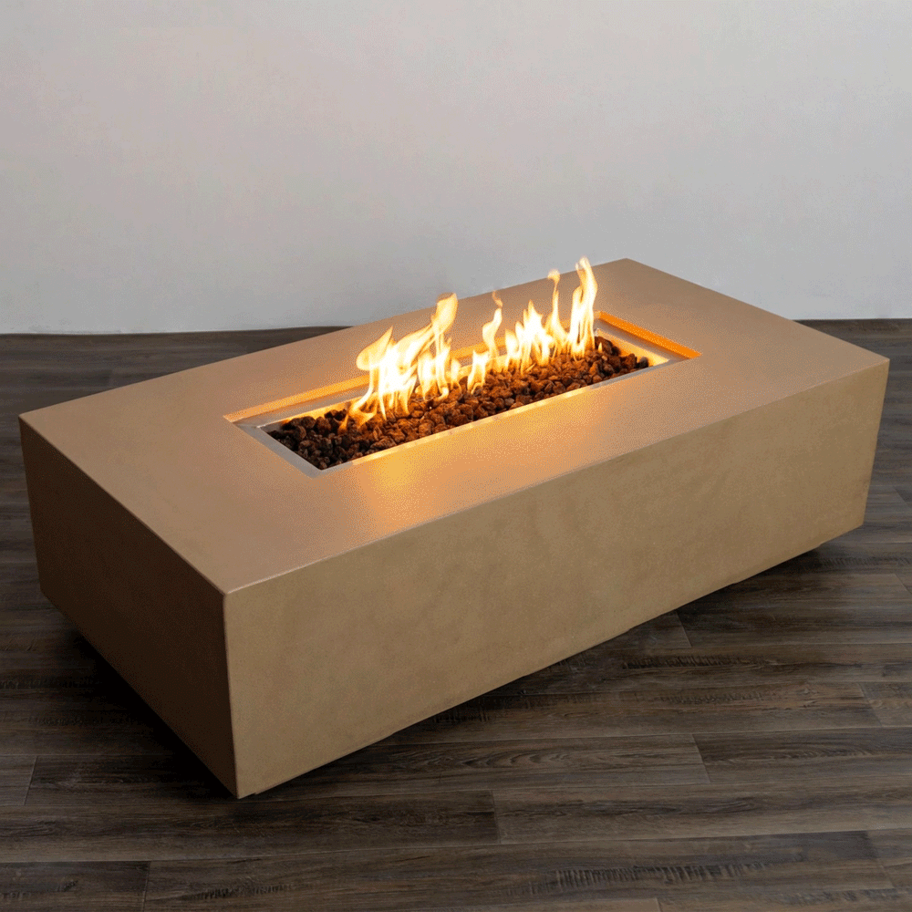 A sand-toned concrete fire pit with sharp rectangular lines rests on a dark wood-look deck, its recessed center channel filled with chunky lava rocks while an even row of bright flames from the gas fire pit rises and moves gently, highlighting the smooth surfaces, low profile, and generous proportions of this modern fire pit design, which reads as a substantial rectangular fire pit that could double as a simple outdoor coffee table when unlit.