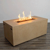 A sand-colored rectangular fire pit with clean, straight sides rests on a dark wood floor against a plain light wall, the smooth blocky body of this concrete fire pit framing a long recessed opening filled with uneven dark lava rocks, where a continuous row of yellow flames rises and bends slightly, the uncluttered studio setting emphasizing the low modern fire pit as the only object in view.