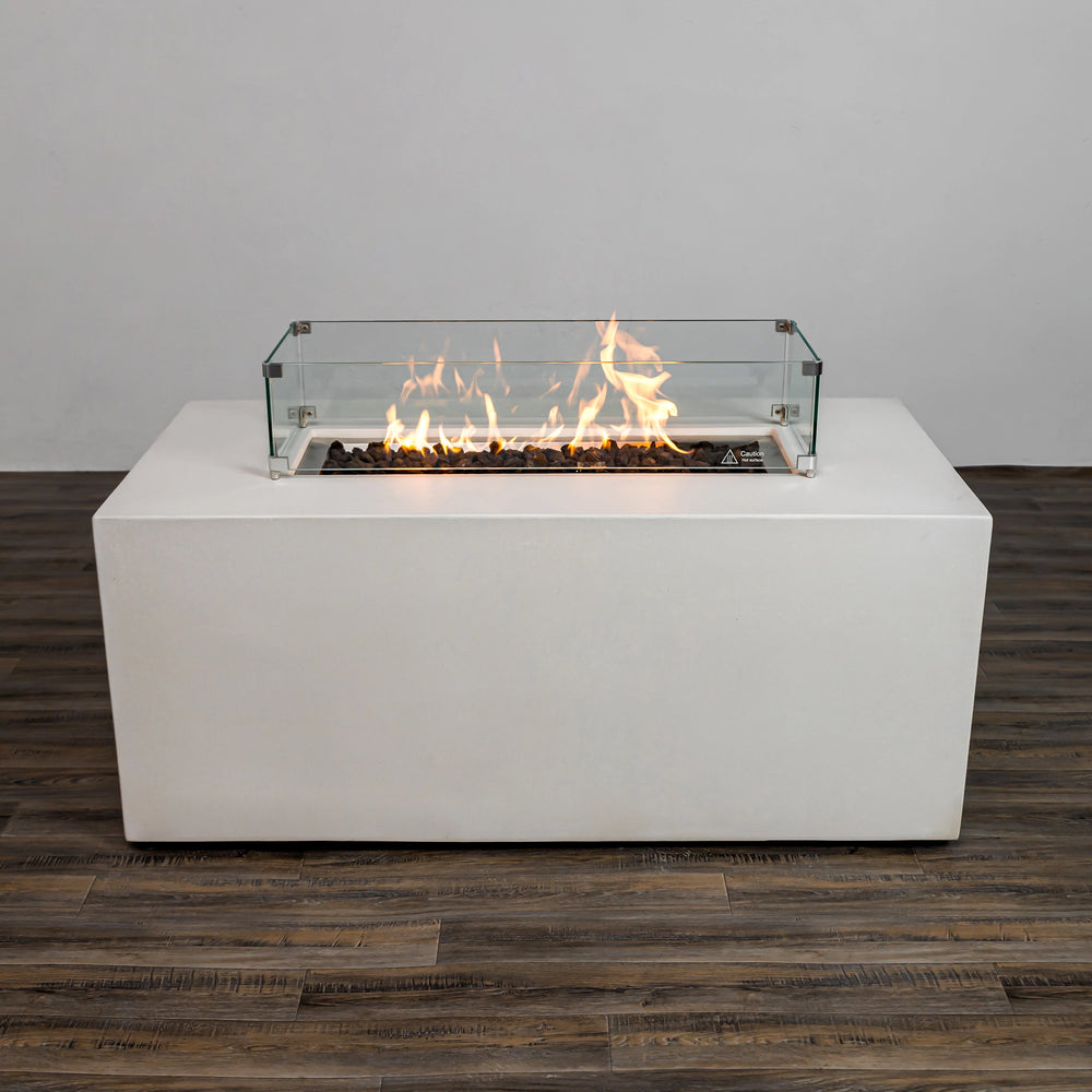 This image highlights the Starfire Designs Beton 55" White Rectangle Hidden Propane Tank Gas Fire Pit with the glass wind guard installed and the flames ignited. The bright, vibrant flames dance over the lava rock filler, creating a warm ambiance. The tempered glass guard enhances safety while adding a stylish accent.