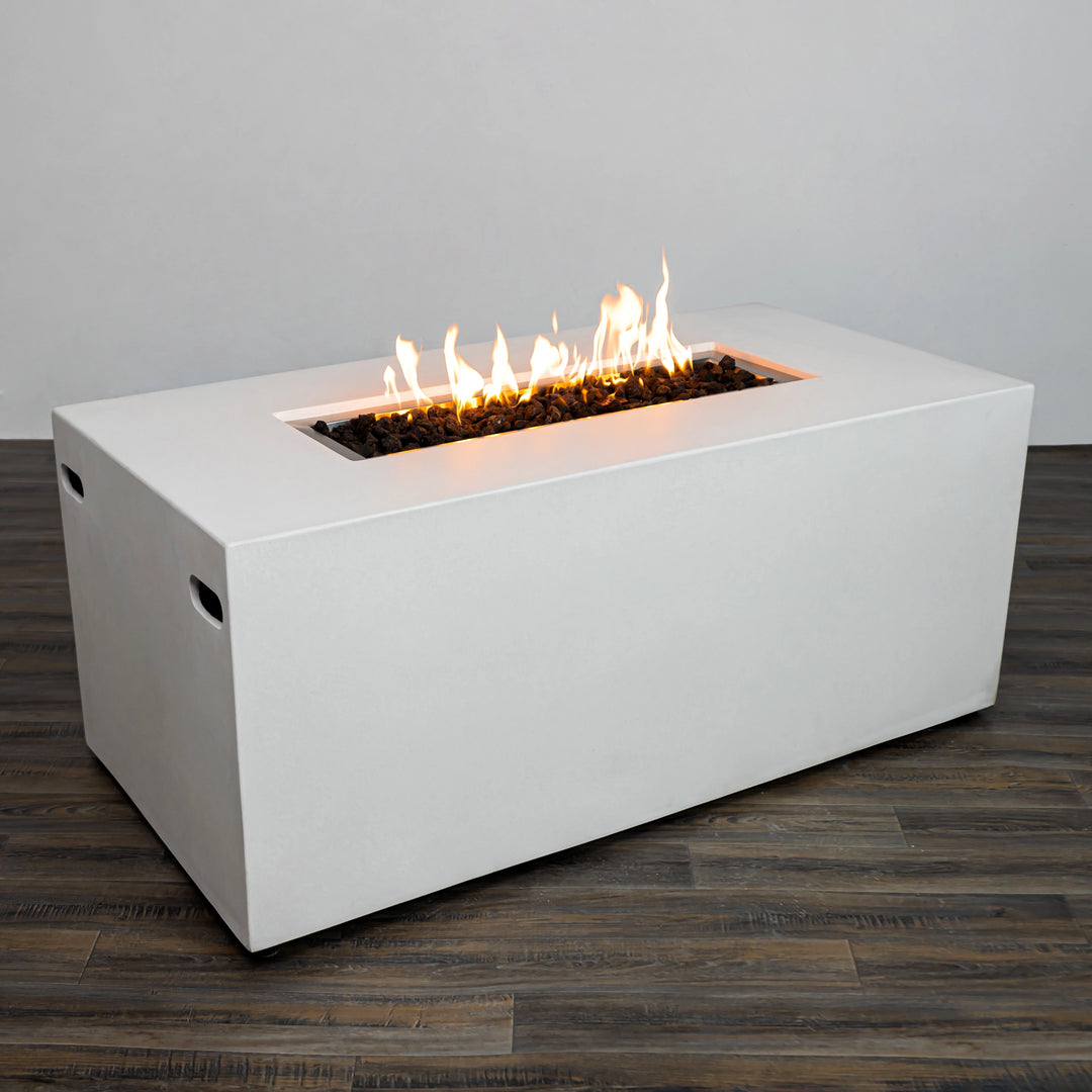 A three-quarter angle of the Starfire Designs Beton 55" White Rectangle Hidden Propane Tank Gas Fire Pit showcasing its sleek edges and generous flame area. The rectangular fire pit features recessed side handles for portability and a white finish for a contemporary look. The fire pit emits a warm glow over decorative lava rocks. 